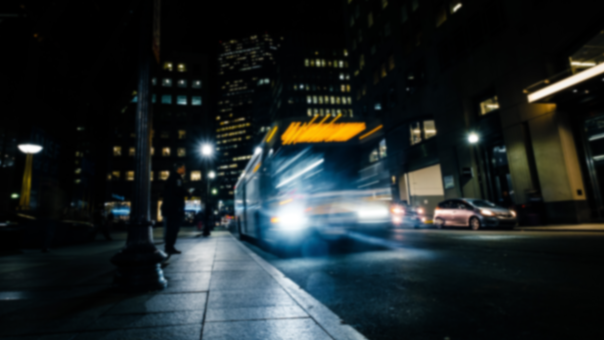 A transit vehicle stops at a bus stop in a nighttime city scene.